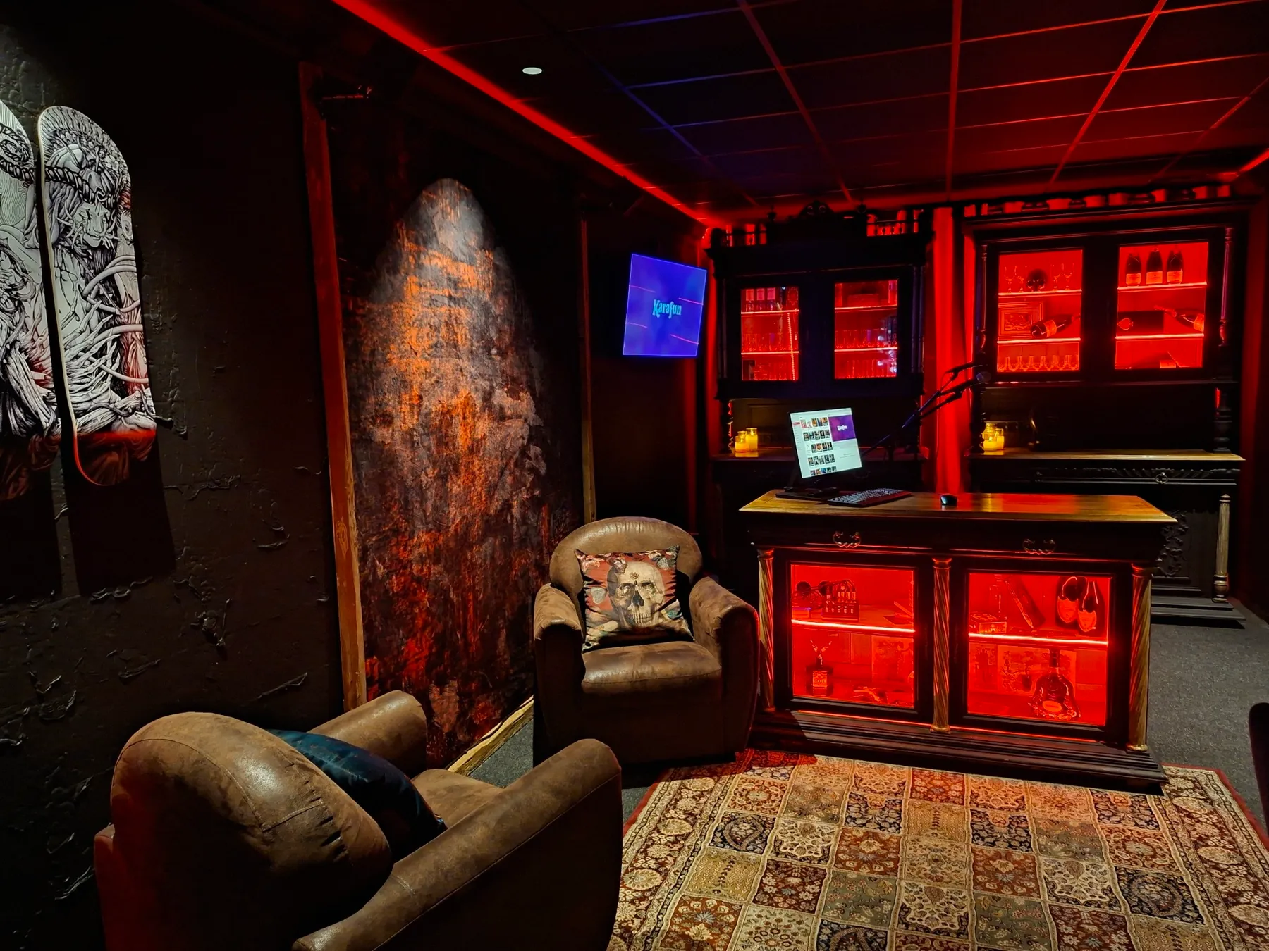 La salle de karaoké : fauteuils en cuir, tapis et meuble bar éclairé de rouge